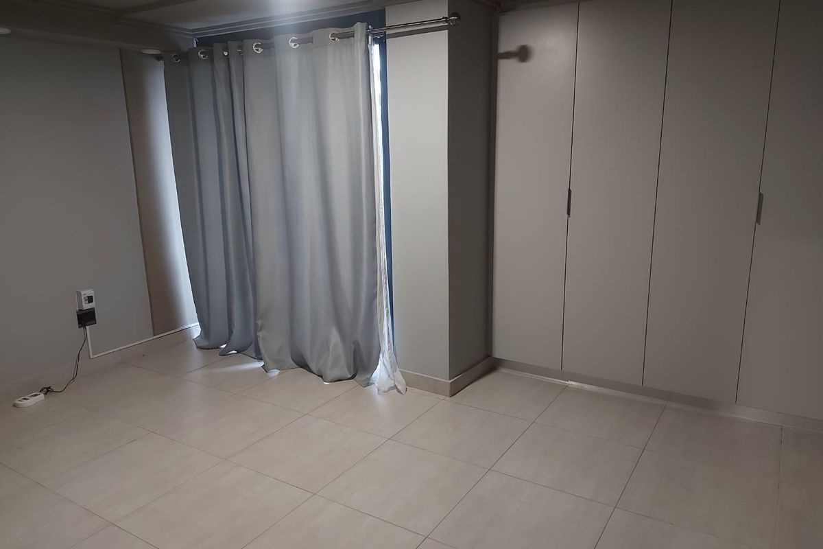 A clean, empty bedroom featuring neutral tiled flooring and ample built-in cupboard storage space.