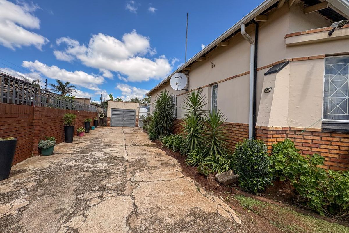 Side view of the property featuring a long concrete driveway, brick boundary wall, and established garden beds along the exterior wall.