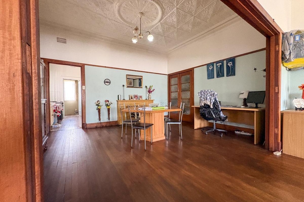 Spacious living area featuring original timber flooring, ornate pressed metal ceilings with a central rose, and classic timber door frames.