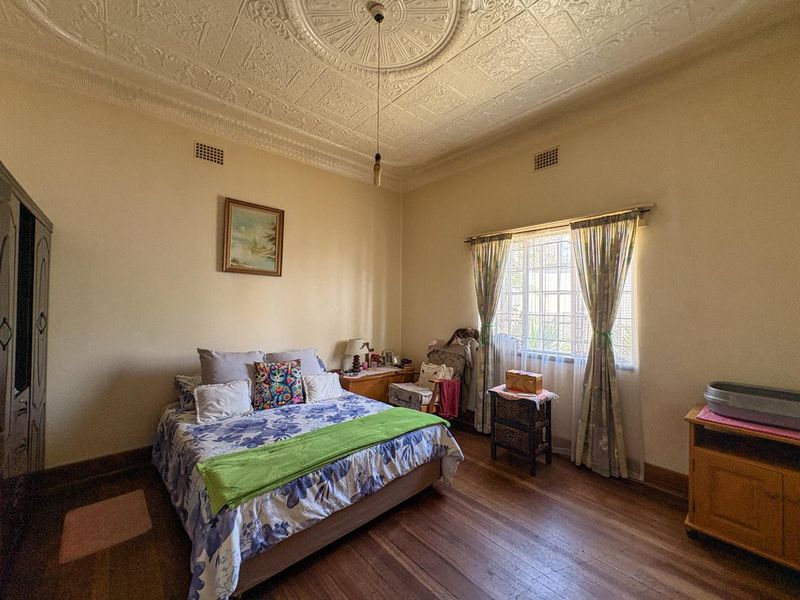A spacious bedroom featuring original timber flooring and a classic ornate pressed metal ceiling with a decorative rose.