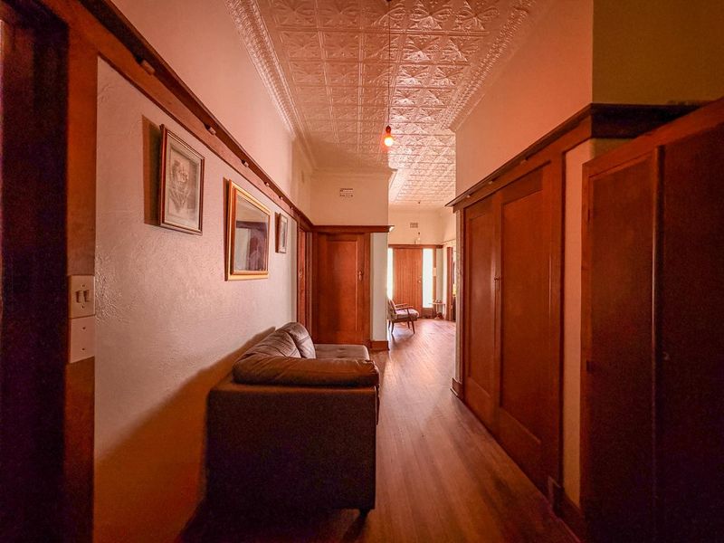 A spacious hallway featuring classic pressed metal ceilings, rich timber wainscoting, and warm timber flooring, connecting multiple rooms throughout the home.