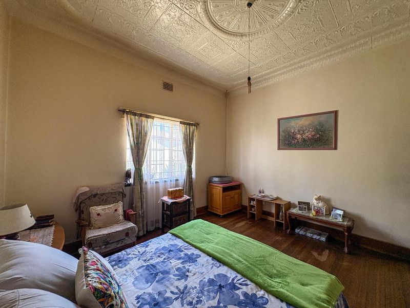 Spacious bedroom featuring original ornate pressed metal ceilings, a decorative ceiling rose, and classic hardwood flooring.