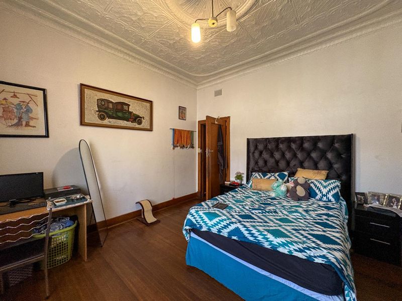 A spacious bedroom featuring original pressed metal ceilings, a decorative ceiling rose, and polished timber flooring.