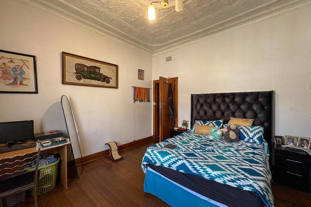 A spacious bedroom featuring original pressed metal ceilings, a decorative ceiling rose, and polished timber flooring.