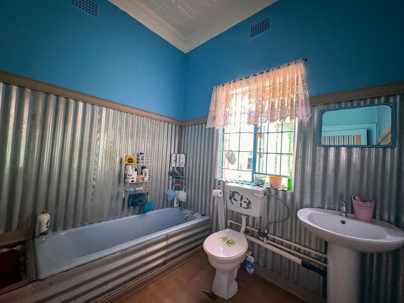A bathroom featuring unique corrugated metal wall cladding, a pedestal basin, and a standard bathtub with exposed plumbing fixtures.