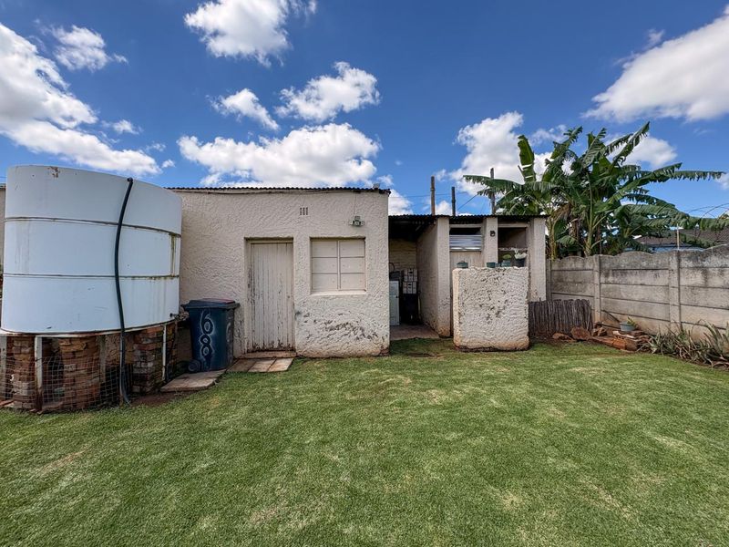 Rear exterior view of the property featuring a large water storage tank, masonry walls, and a small garden area with a precast boundary wall.