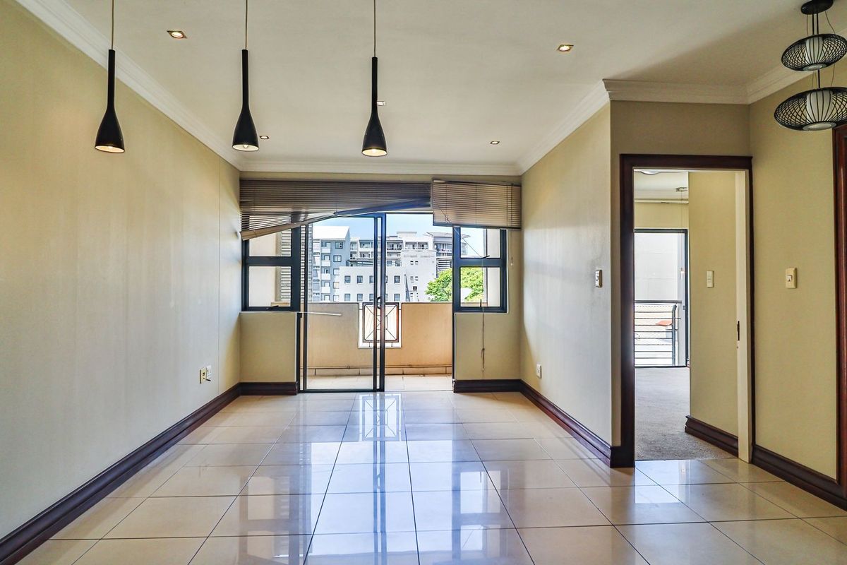 Spacious, empty living area featuring polished porcelain floor tiles, modern pendant lighting, and direct access to a private balcony through sliding glass doors.