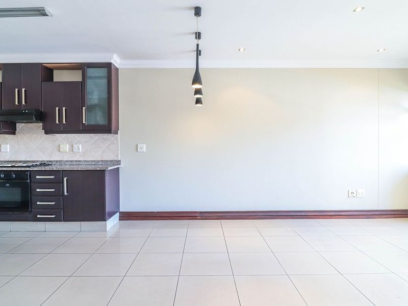 An open-plan living and kitchen area featuring dark wood cabinetry, granite countertops, tiled flooring, and modern lighting fixtures in a clean, vacant space.