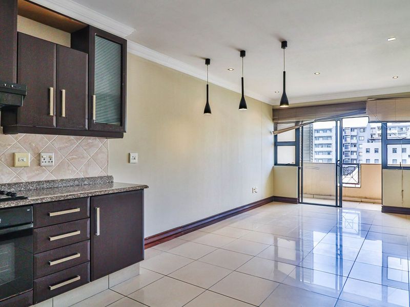 Spacious open-plan kitchen and living area featuring dark wood cabinetry, granite countertops, tiled floors, and direct access to a private balcony.