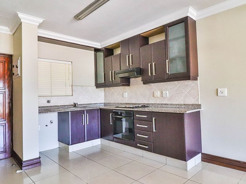 A functional kitchen featuring dark wood cabinetry, granite countertops, built-in oven, hob, and extractor fan, with tiled flooring and backsplash.