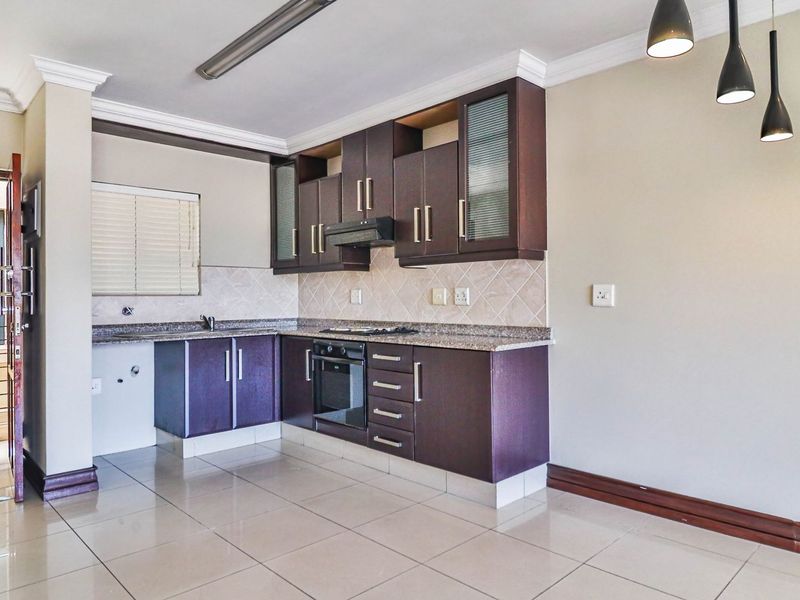 A clean, empty kitchen featuring dark wood cabinetry, granite countertops, built-in oven, hob, extractor fan, and neutral tiled flooring.
