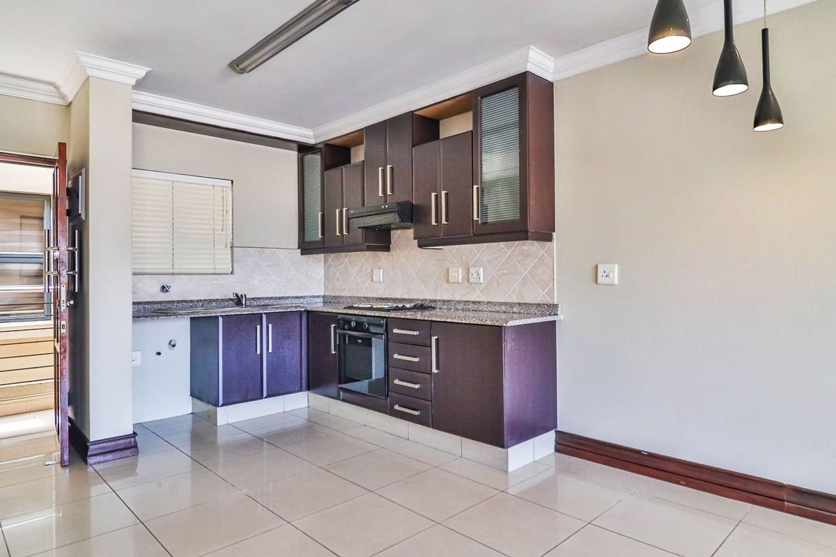 A clean, empty kitchen featuring dark wood cabinetry, granite countertops, built-in oven, hob, extractor fan, and neutral tiled flooring.