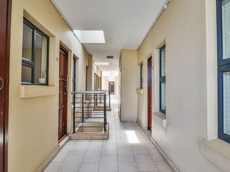 A well-lit, tiled apartment hallway featuring metal balustrades, skylights, and multiple access doors to individual units.