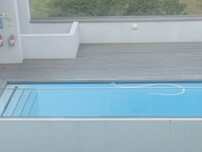 An elevated view of a swimming pool area featuring modern timber decking and a clear glass balustrade overlooking the surroundings.