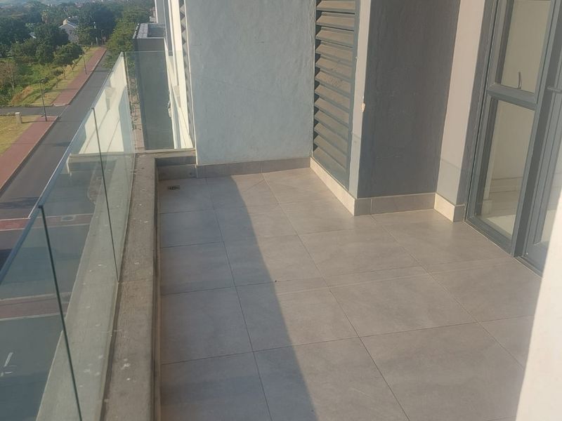 A modern apartment balcony featuring tiled flooring, a sleek glass balustrade, and a louvred privacy screen with views of the surrounding area.