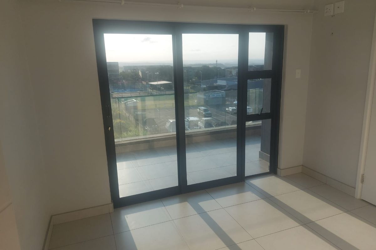 An empty, well-lit living area featuring neutral tiled flooring and large sliding glass doors that provide access to a balcony with exterior views.