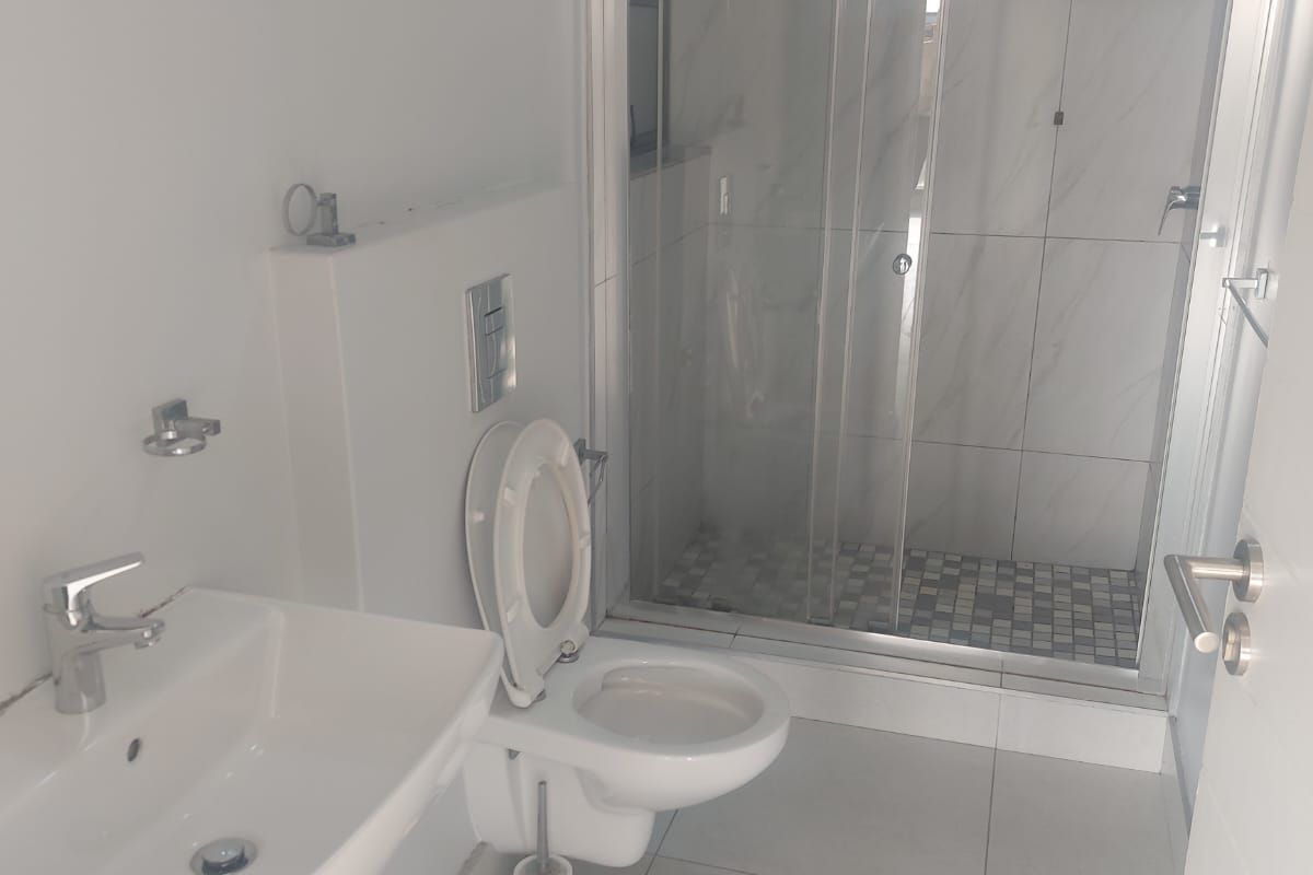 A clean, modern bathroom featuring a wall-mounted toilet, a basin with a mixer tap, and a glass-enclosed shower with tiled finishes.