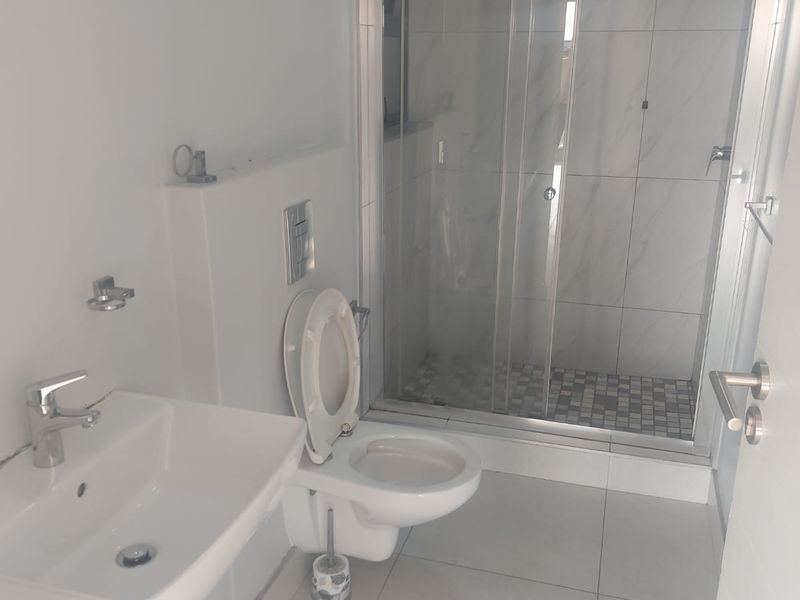 A clean, modern bathroom featuring a wall-mounted toilet, a basin with a mixer tap, and a glass-enclosed shower with tiled finishes.