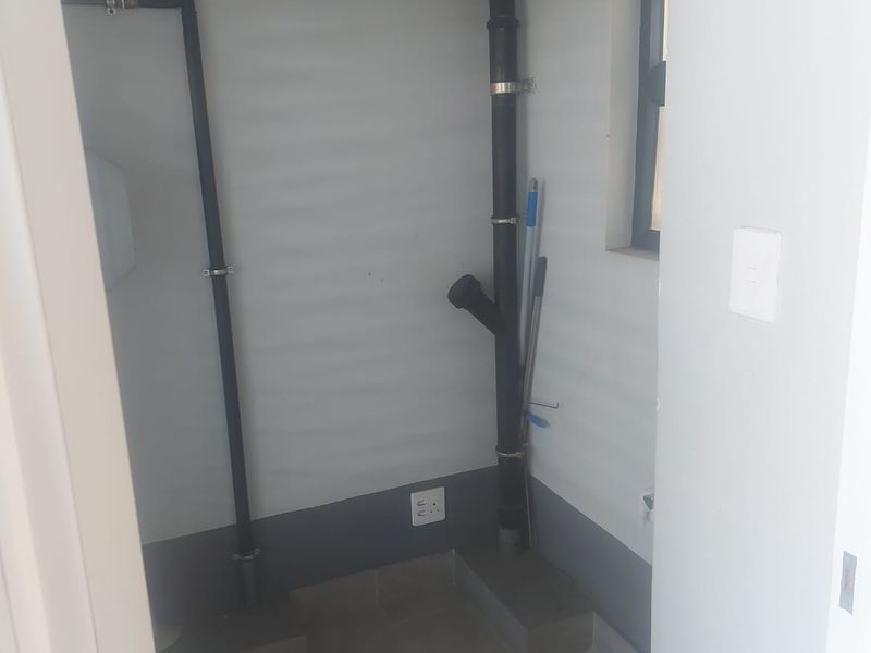 A small, functional laundry or utility space featuring tiled flooring and exposed plumbing infrastructure, suitable for appliance installation.