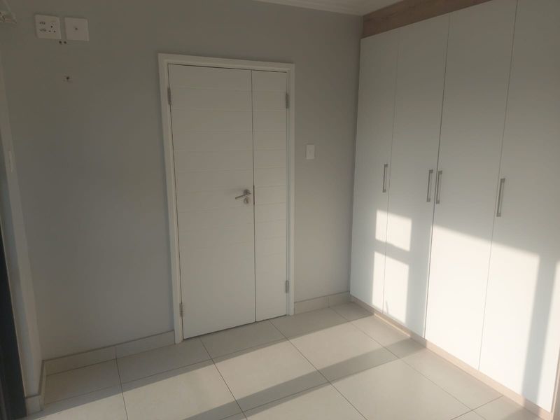 A clean, empty bedroom featuring neutral tiled flooring and modern white built-in cupboards, offering a bright and versatile living space.