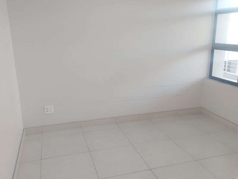 A bright, empty bedroom featuring neutral tiled flooring and a modern aluminium-framed window, providing a clean canvas for interior design.