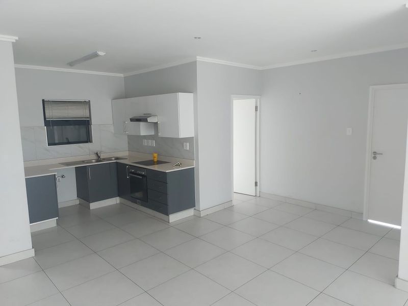 Modern open-plan kitchen and living area featuring sleek cabinetry, integrated appliances, neutral tiled flooring, and clean finishes throughout.