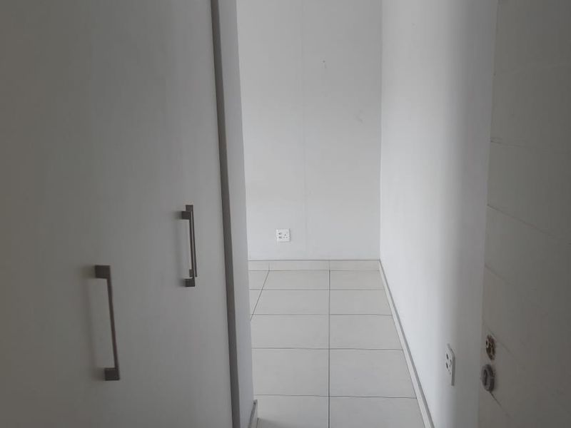 A clean, empty hallway featuring neutral tiled flooring and built-in storage cupboards, providing a bright and functional transition space within the apartment.