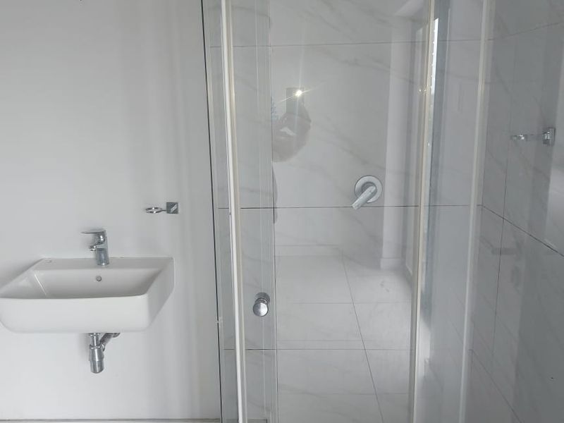 A modern, clean bathroom featuring a wall-mounted basin with chrome fixtures and a glass-enclosed shower with tiled finishes.