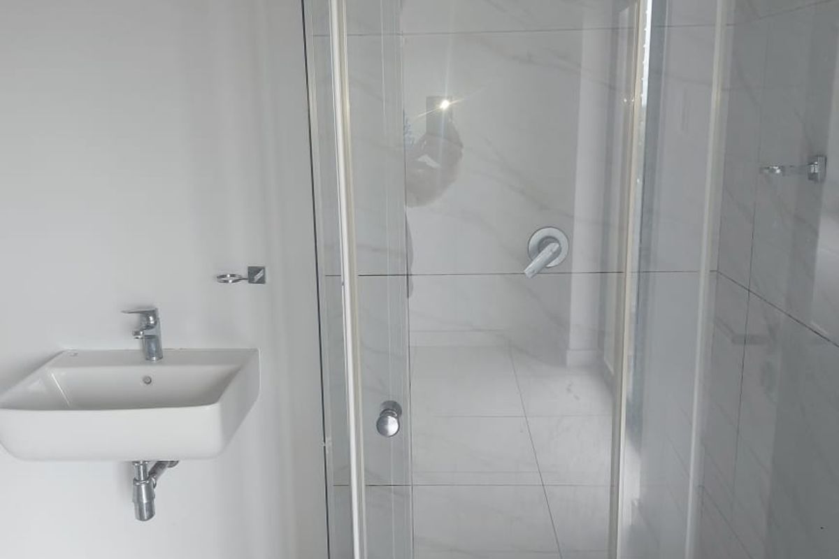A modern, clean bathroom featuring a wall-mounted basin with chrome fixtures and a glass-enclosed shower with tiled finishes.