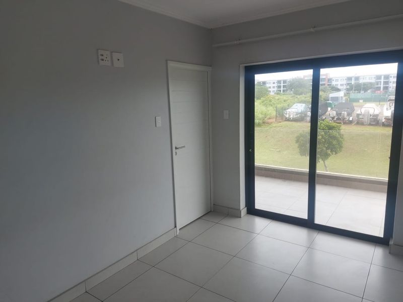 A bright, empty living area featuring neutral tiled flooring and a large sliding glass door providing access to an outdoor patio space.