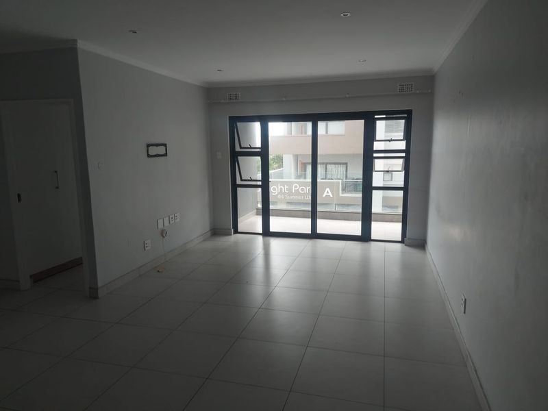 An empty, open-plan living area featuring neutral tiled flooring, recessed lighting, and large sliding glass doors leading to a balcony.