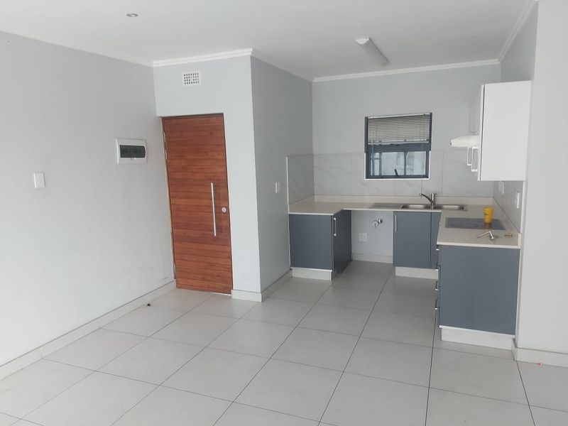 Open-plan kitchen and living area featuring modern grey cabinetry, tiled flooring, and a timber entrance door in a clean, neutral space.