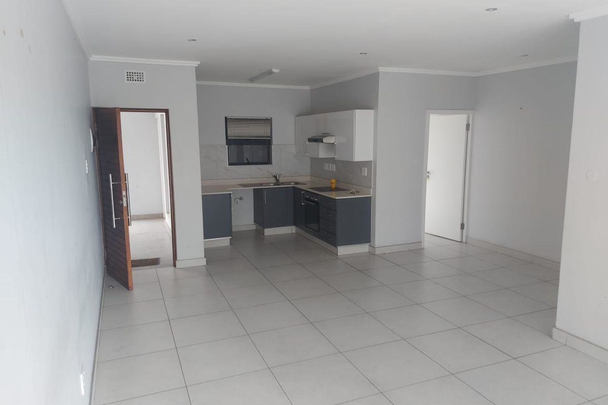 Spacious open-plan living area featuring a modern kitchen with built-in cabinetry, integrated appliances, and neutral tiled flooring throughout.