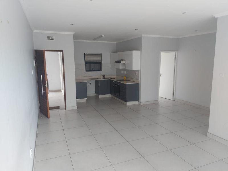 Spacious open-plan living area featuring a modern kitchen with built-in cabinetry, integrated appliances, and neutral tiled flooring throughout.