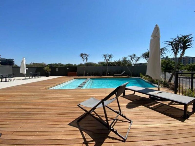 A well-maintained outdoor pool area featuring timber decking, a clear swimming pool, and secure boundary walling.