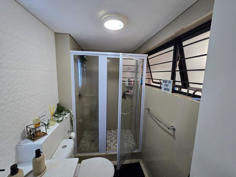 A functional bathroom featuring a glass-enclosed shower, tiled walls, and a top-hung window for ventilation.