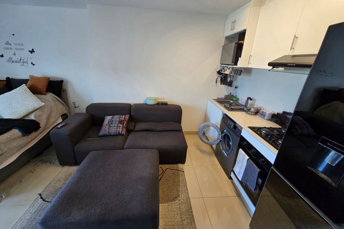 Compact open-plan studio apartment featuring a functional kitchenette with built-in appliances and tiled flooring throughout.