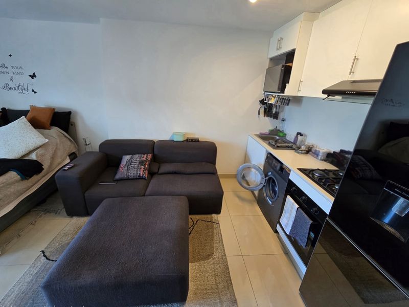 Compact open-plan studio apartment featuring a functional kitchenette with built-in appliances and tiled flooring throughout.