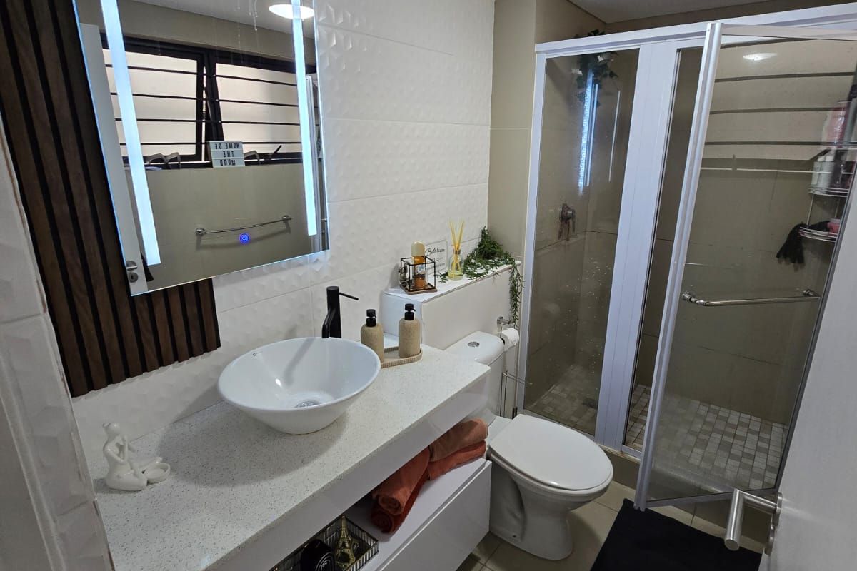 Modern bathroom featuring a vessel sink on a floating vanity, LED backlit mirror, and a glass-enclosed shower with neutral tiled finishes.