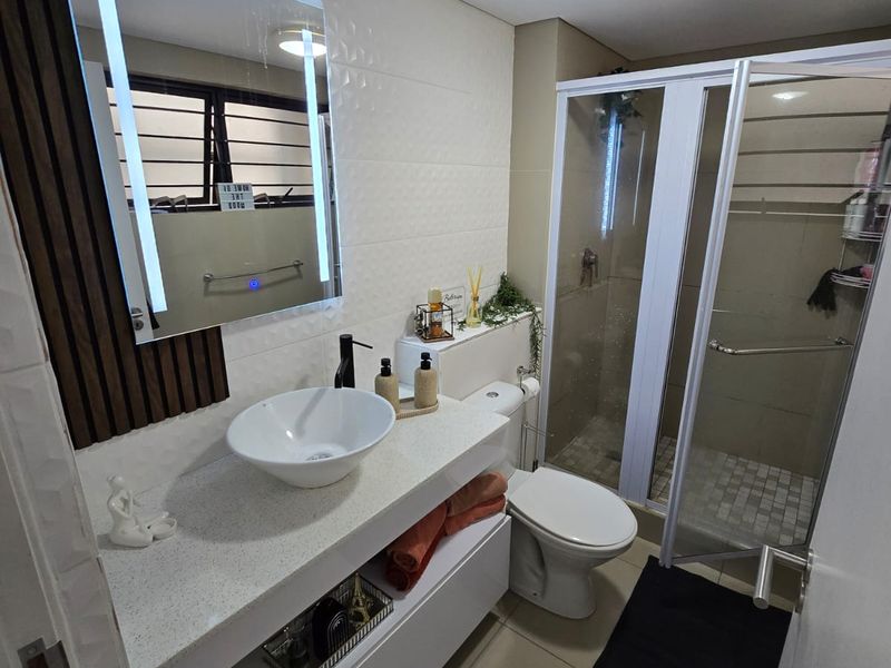 Modern bathroom featuring a vessel sink on a floating vanity, LED backlit mirror, and a glass-enclosed shower with neutral tiled finishes.