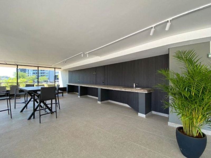 A spacious covered balcony featuring a modern built-in bar counter with a sink, sleek slatted wall paneling, and contemporary track lighting.