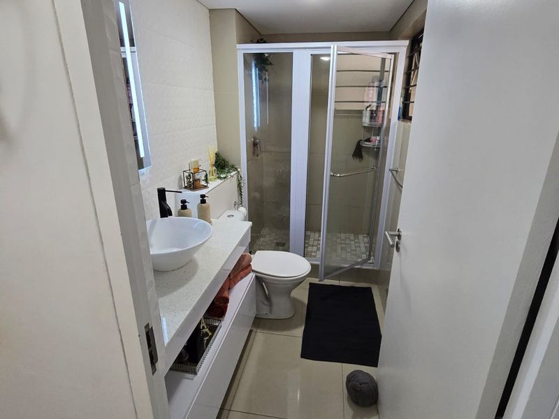 A modern bathroom featuring a sleek vanity with a vessel sink, a glass-enclosed shower, and neutral floor-to-ceiling tiling.