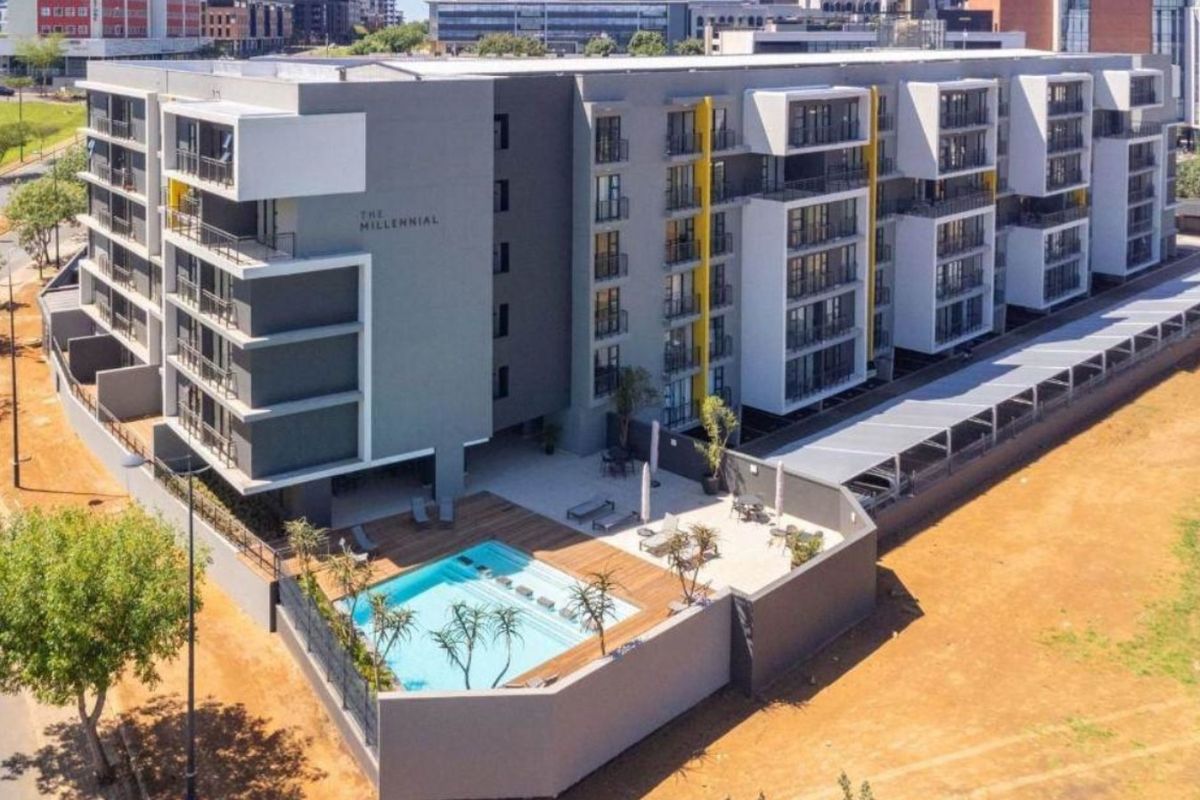 Aerial view of The Millennial apartment complex featuring a modern building design, swimming pool with timber decking, and secure perimeter fencing.