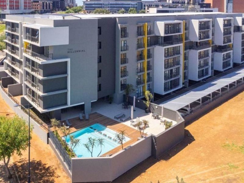 Aerial view of The Millennial apartment complex featuring a modern building design, swimming pool with timber decking, and secure perimeter fencing.