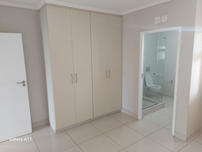 A clean, neutral bedroom featuring built-in cupboards, tiled flooring, and direct access to an en-suite bathroom.