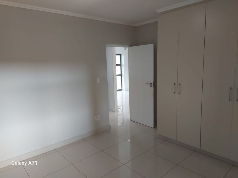 A clean, empty bedroom featuring neutral tiled flooring and ample built-in cupboard storage, leading to an adjacent hallway.