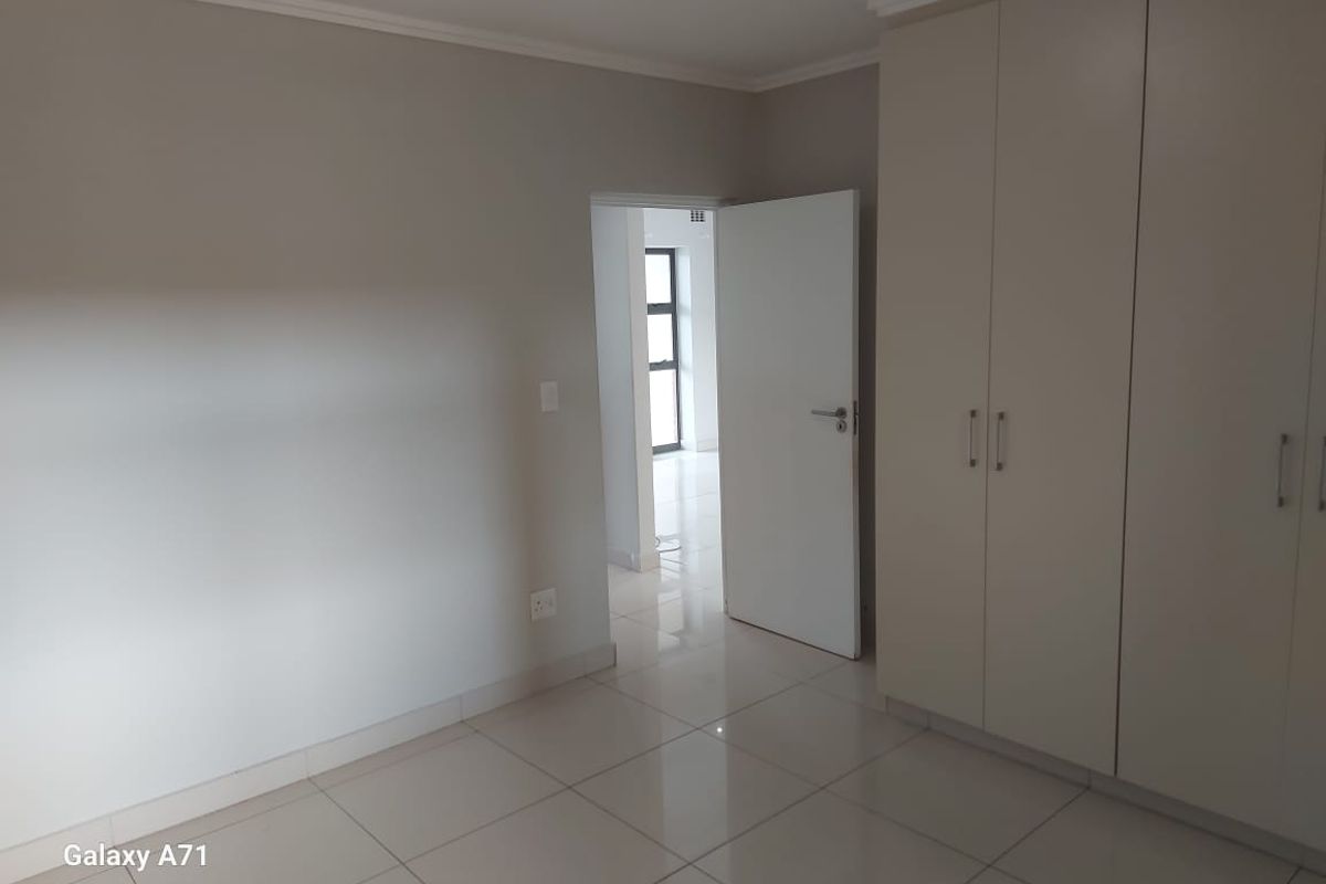 A clean, empty bedroom featuring neutral tiled flooring and ample built-in cupboard storage, leading to an adjacent hallway.