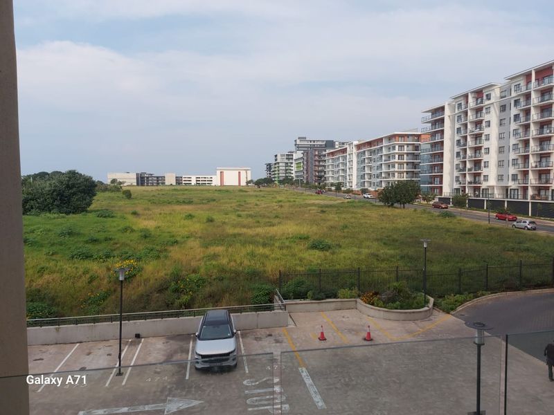 An elevated view overlooking a parking area, open green space, and surrounding apartment buildings in the neighbourhood.