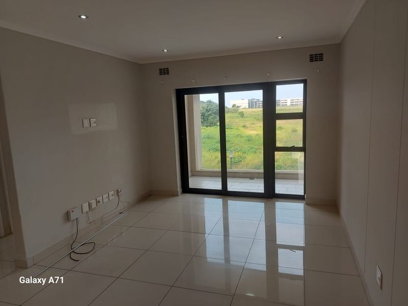 A bright, empty living area featuring polished tile flooring, recessed lighting, and large sliding glass doors leading to an outdoor balcony.