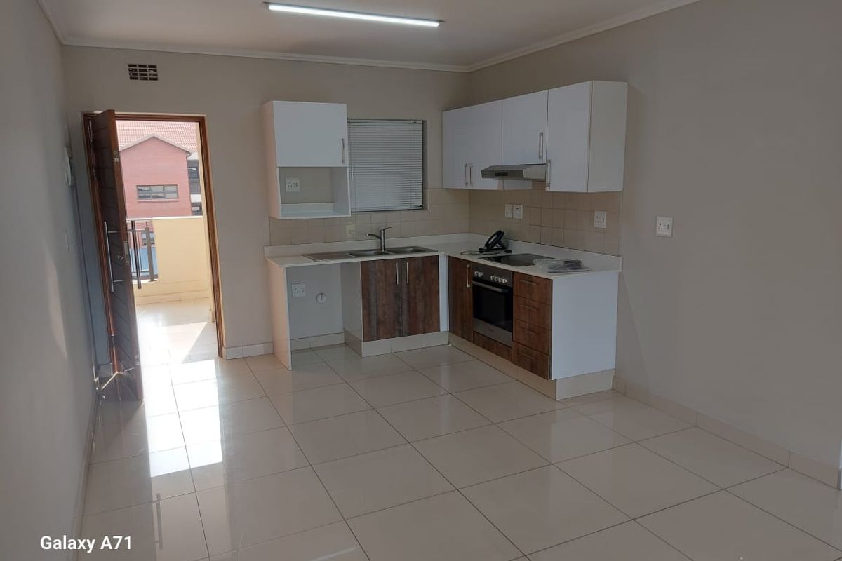 A clean, modern kitchen featuring built-in cabinetry, a stainless steel sink, an integrated oven, and a hob, with neutral tiled flooring throughout.
